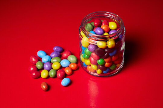 Still life multicolored candy in glass jar on red background
