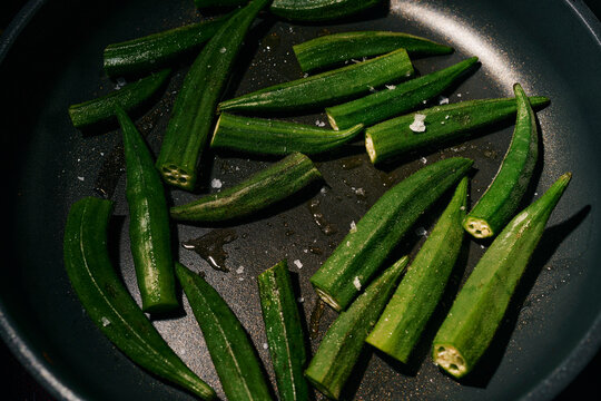 Vibrant green okra cooking in oil and salt in frying pan
