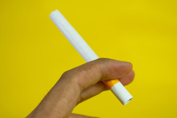 A man hand holds a handmade cigarette on yellow background