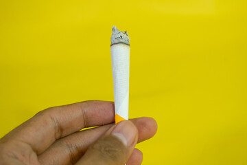 A man hand holds a handmade cigarette on yellow background