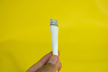 A man hand holds a handmade cigarette on yellow background - obrazy, fototapety, plakaty