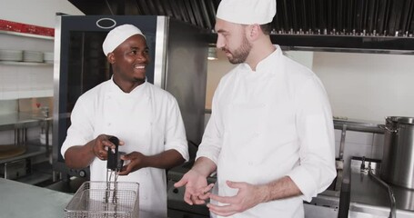 Focused diverse male chef instructing trainee male chef in kitchen, slow motion
