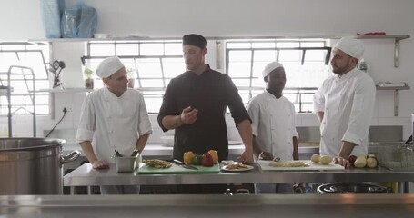 Diverse male chef instructing group of trainee male chefs in kitchen, slow motion