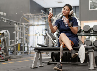 Confident woman with artificial leg sits relax after exercising in fitness gym. Prosthetic limb strengthen physical injury amputee. Asian female with mechanical prosthesis leg workout for wellbeing.