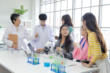 Group of Asian secondary students have fun in science laboratory class with senior 60s teacher wearing lab coat, experience science specialist healthy woman apply job working in modern private school