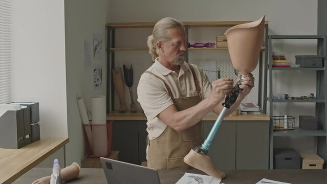 Zoom in shot of mid aged Caucasian male manufacturing worker assembling leg prosthesis using hex key, working alone in small workshop