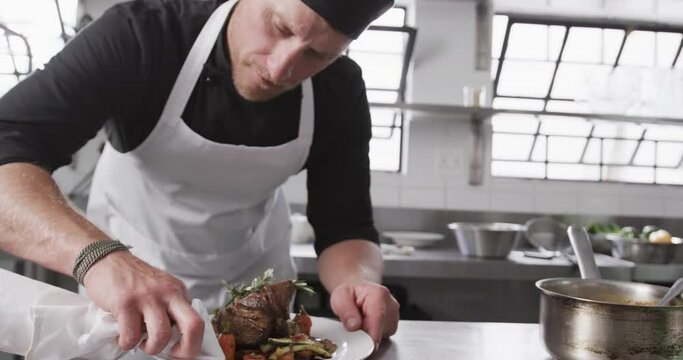 Caucasian male chef cleaning plate with meal in kitchen, slow motion