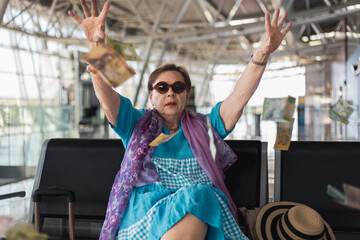 Rich tourist senior woman sitting on the bench in airport hall waiting for her flight throwing money in the air