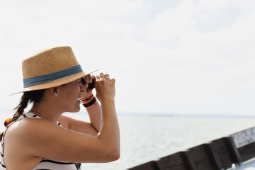 A young woman in a hat, sitting on a boat, using a telescope to look toward the ocean horizon