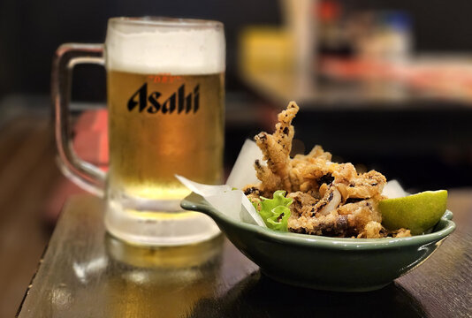 BANGKOK, THAILAND - SEPTEMBER 28, 2023: Ika Geso Karaage or Deep Fried Squid Tentacles with Asahi Beer background on Wood Table in japanese restaurant. It is distributed by Asahi Breweries, Ltd.