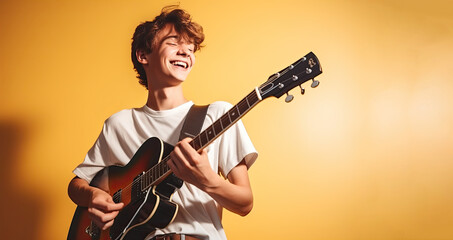 Happy teenage boy playing the guitar on a yellow background. Place for text