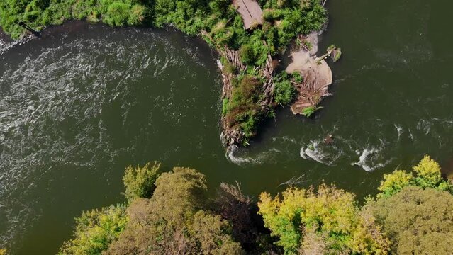 Flying along a beautiful river with rapids and curved banks. Early fall or summer. View from above vertically