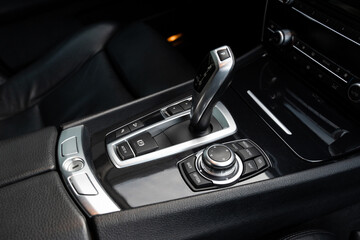 Black leather car interior with modern gear shift lever and control buttons for multimedia...