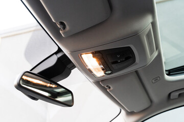 Close up of rearview mirror, light sensor and grey ceiling inside new modern car. Details in...