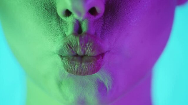 Extreme Close Up Of A Beautiful Woman Lip While She Symbolizes A Kiss Into The Camera With Green Purple Background In Slow Motion