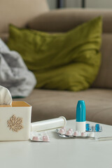 Cold medicine on the background of a sofa with pillows and a blanket. Tablets, spray and thermometer are on the table