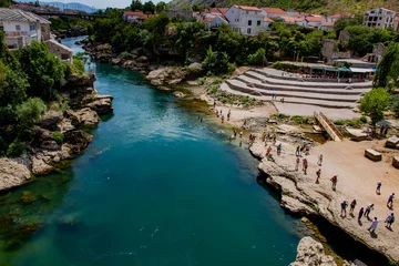 Papier Peint photo Stari Most Tourists or visitors or people spending time on the Neretva River bank or side, Mostar, Bosnia and Herzegovina