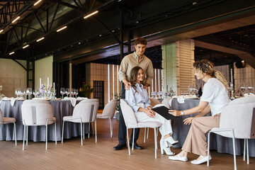 event manager showing clipboard with contract to happy couple in banquet hall with festive tables
