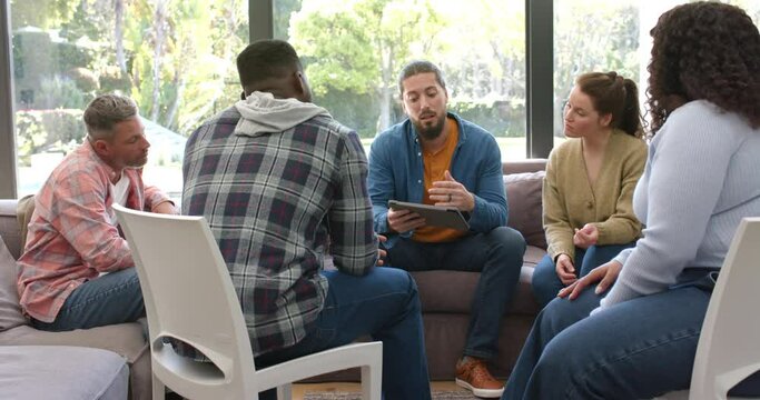 Diverse group of friends and male therapist with tablet in group therapy session
