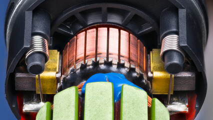 Closeup of electric DC motor rotor with copper winding fixed by blue epoxy in black plastic housing. Commutator with carbon brush contacts pressed by steel cylindric coil springs inside engine detail. - 654295596