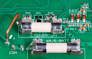 Closeup of ceramic tubes of electrical fuses in metal holder on circuit board. Low ohm wire resistor to current measuring, capacitors or red diodes. Surface mounted electronic components on green PCB.