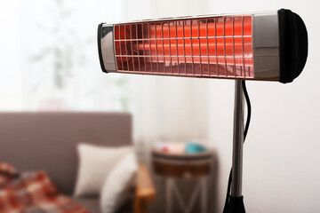 Electric infrared heater warming up living room with sofa and potted plant at background