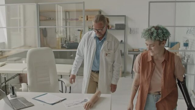 Medium shot of young Caucasian woman with bionic arm having appointment with adult male prosthetist in his bright contemporary office