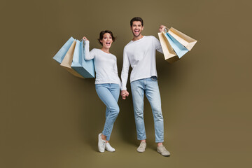 Full length photo of excited funky married couple wear white shirts rising bargains isolated brown...
