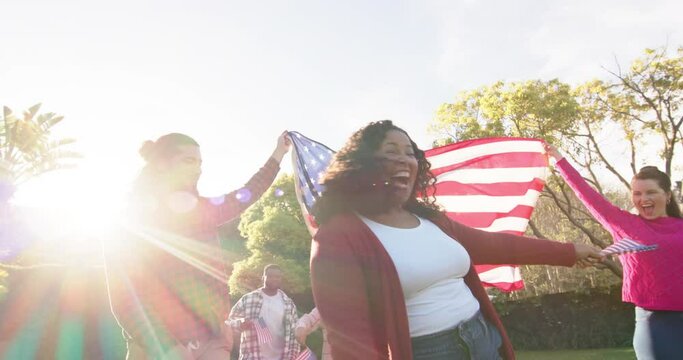 Happy diverse male and female friends dancing with flags in sunny garden