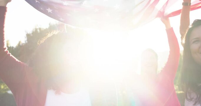 Happy diverse male and female friends dancing with flags in sunny garden