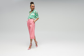 stylish african american woman in pink sunglasses and stylish attire posing on grey backdrop
