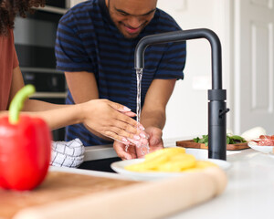 Couple At Home With Man With Down Syndrome And Woman Washing Hands Before Preparing Meal In Kitchen