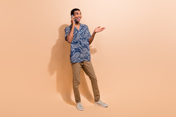 Fototapeta premium Full length photo of excited dreamy man wear print shirt communicating modern gadget empty space isolated beige color background