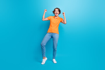 Full length photo of overjoyed funny woman wear orange t-shirt raising fists up scream yes win lottery isolated on blue color background