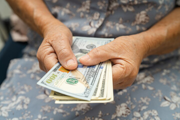 Asian senior woman holding and counting US dollar banknotes money in purse. Poverty, saving problem...