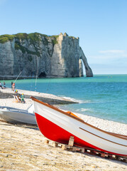 A red boat standing on the seashore with elephant like sea cliff in the background in Étretat