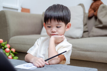 Naklejka premium Asian boy holding pencil and showing bored face while studying online on laptop