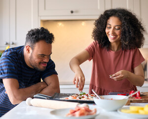 Couple At Home With Man With Down Syndrome And Woman Putting Toppings On Pizza In Kitchen Together