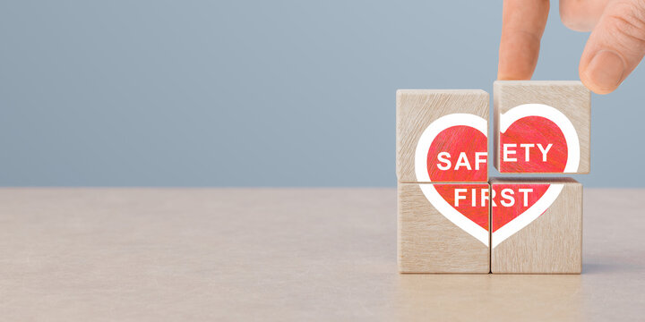 Safety first, heart shaped icon on wooden cubes in human hand. work safety, caution work hazards, danger surveillance, zero accident concept. Employees safety awareness at workplace. Safety banner.