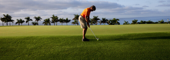 The golfer practices on the putting green with a golf iron, at first light in the morning.