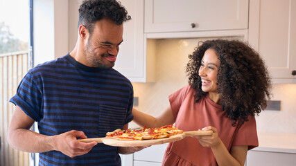 Couple At Home With Man With Down Syndrome And Woman Holding Homemade Pizza In Kitchen Together