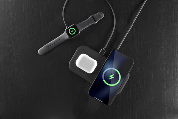 Wireless charging for a smartphone, headphones and watch, on a black background, on a table, top view.