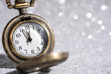 A vintage clock on a blurred shiny background reads five minutes to twelve. A concept for the new year.
