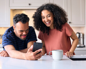 Couple At Home With Man With Down Syndrome Looking At Mobile Phone Together