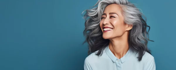 Fotobehang Psychology portrait of a confident beautiful Asian woman in her 50s. Middle-aged woman with a short gray hair. Photo with copy space on blue background. Format photo 5:2. © Stavros