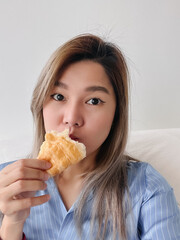 Asian Thai office woman take selfie while enjoy eating croissant at apartment.