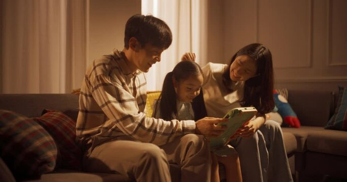 저녁에 소파에 앉아 태블릿으로 비디오 게임을 하는 아빠, 엄마, 딸의 와이드 샷