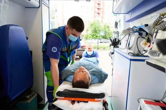 Paramedics in uniform unload a gurney with patient from ambulance