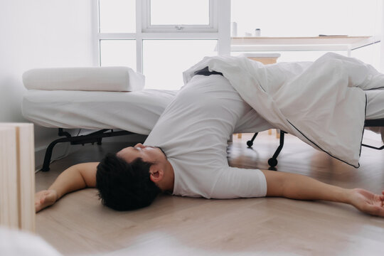 Asian man sleeping lying on floor, having deep sleep dream, fall down from white bed at apartment.