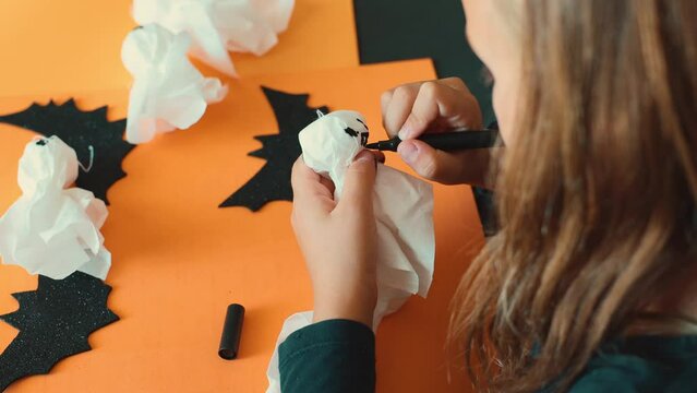 Child making ghost from napkins decoration for Halloween party, preparation home DIY paper garland. Zero waste. Do it yourself, handmade creativity craft, holiday. Education hobby children development